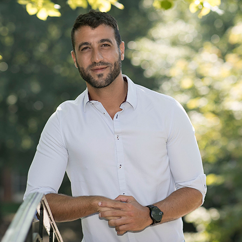 Photo of David Nemer from the waist up, surrounded by green foliage.