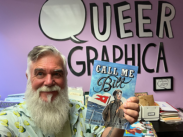 James Miller holds up a book titled Call Me Bill with the words Queer Graphica written on the wall behind him.