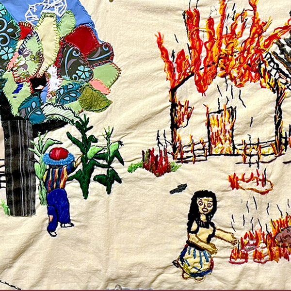 A piece of embroidered fabric showing a village on fire and under attack from a military helicopter.