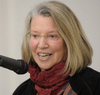 A headshot of Nancy Fraser wearing a red scarf and speaking into a microphone.