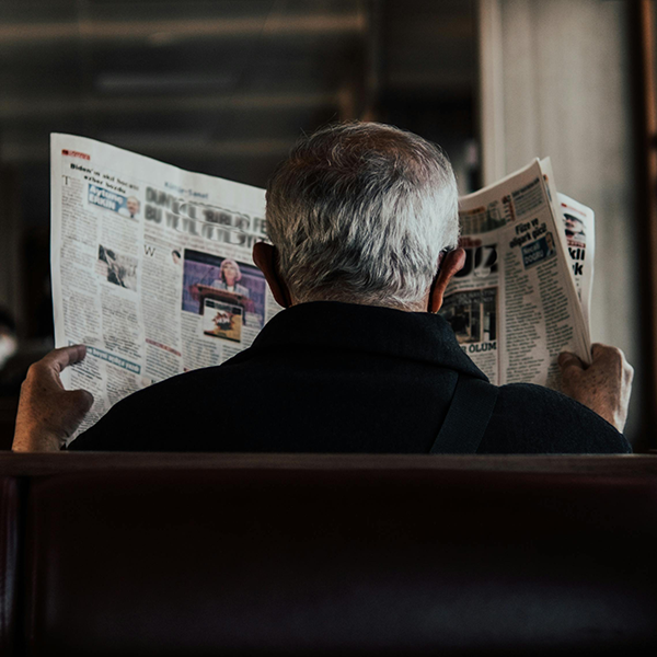 Gray-haired man facing away reading a newspaper.