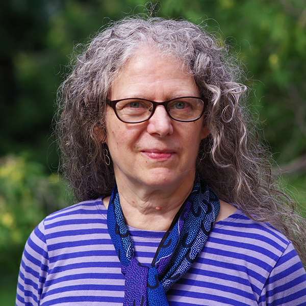 Headshot of Pam McKenzie standing outside against a green, bushy backdrop.