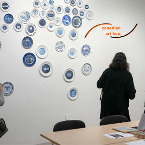 Visitors in front of 'The Immigrants: Canada 150' by Soheila Esfahani- a series of plates with blue and white labels hung on the wall in a specific pattern. 