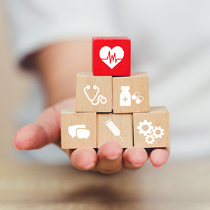 Hand holds a series of wooden blocks showing different healthcare icons