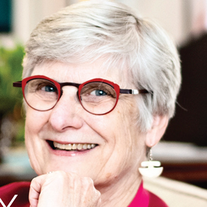 White woman with short grey hair and red frame glasses smiling